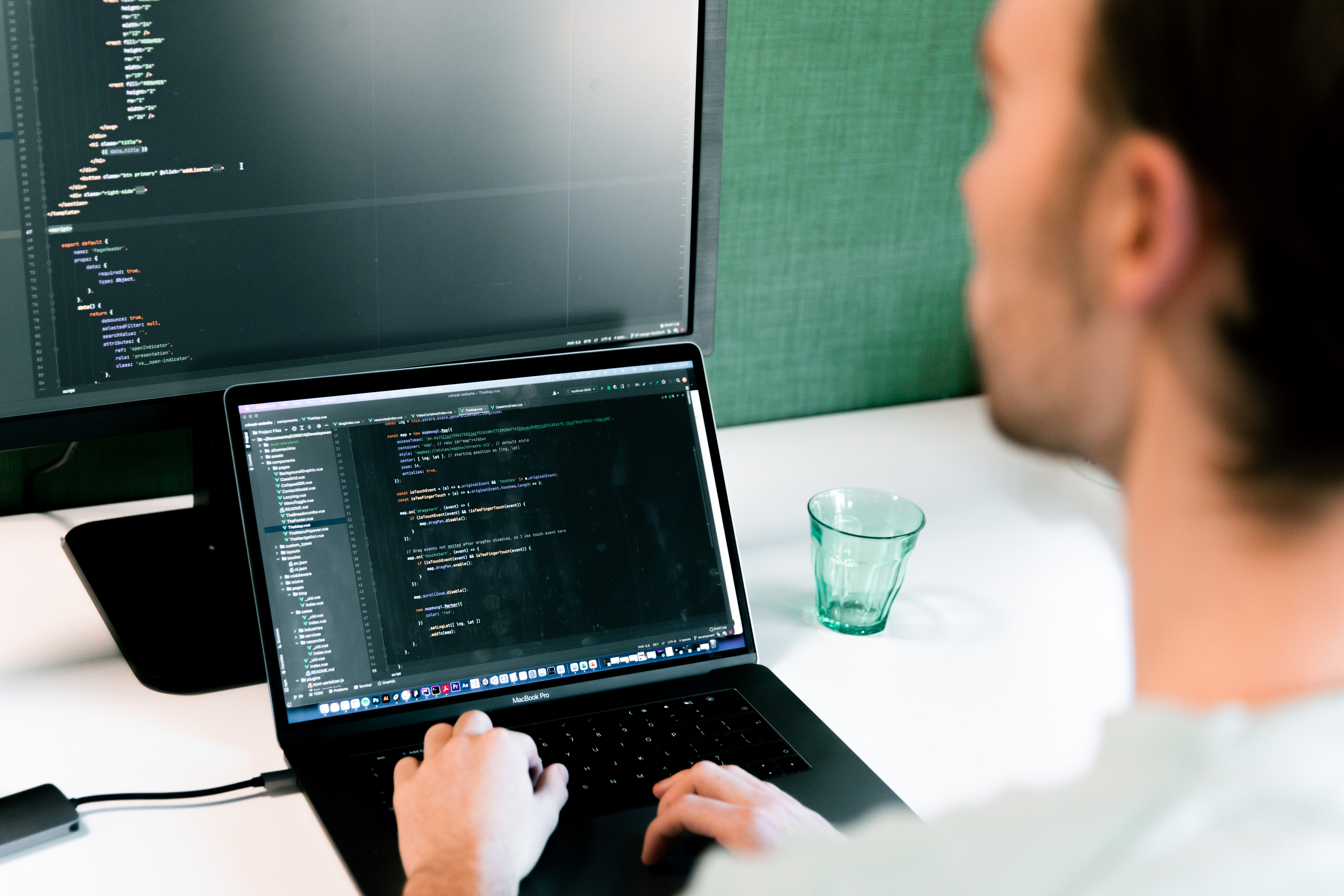 Person working on a laptop with programming code displayed on both the laptop and an external monitor.
